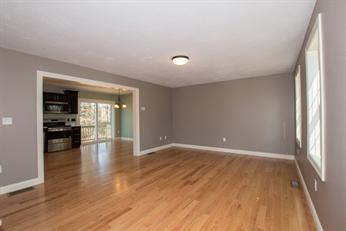 Empty living room with hardwood floors, gray walls, and view into kitchen and dining area.