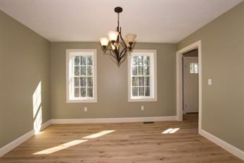 Empty room with light wood floor, olive walls, two windows, and a ceiling light fixture.