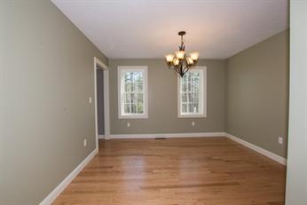 Empty room with hardwood floors, beige walls, two windows, and a chandelier.
