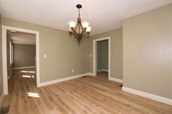 Empty room with light wood floors, beige walls, and a chandelier hanging from the ceiling.