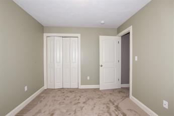 Empty beige bedroom with carpet, closed closet doors, and an open door to a hallway.