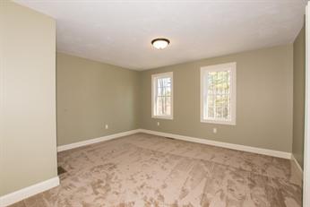 Empty carpeted room with beige walls, two windows, and a ceiling light fixture.