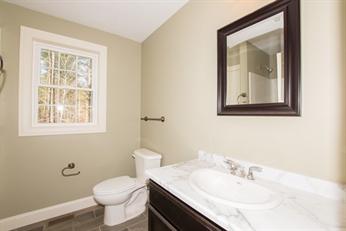 Bathroom with a toilet, sink, mirror, towel ring, and window on a beige wall.