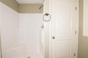 White shower with a built-in seat next to a closed white door and beige walls.