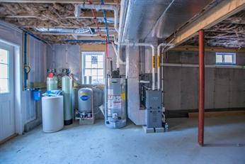Unfinished basement with water softener, water heater, furnace, and exposed pipes.