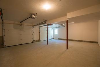 Empty, spacious garage with two closed doors, concrete floor, and a window in the back.