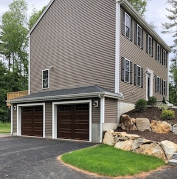 Two-car garage attached to a brown, two-story house with landscaped rocks and shrubs.