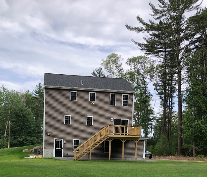 Three-story house with beige siding, a deck, and stairs, surrounded by trees and grass.
