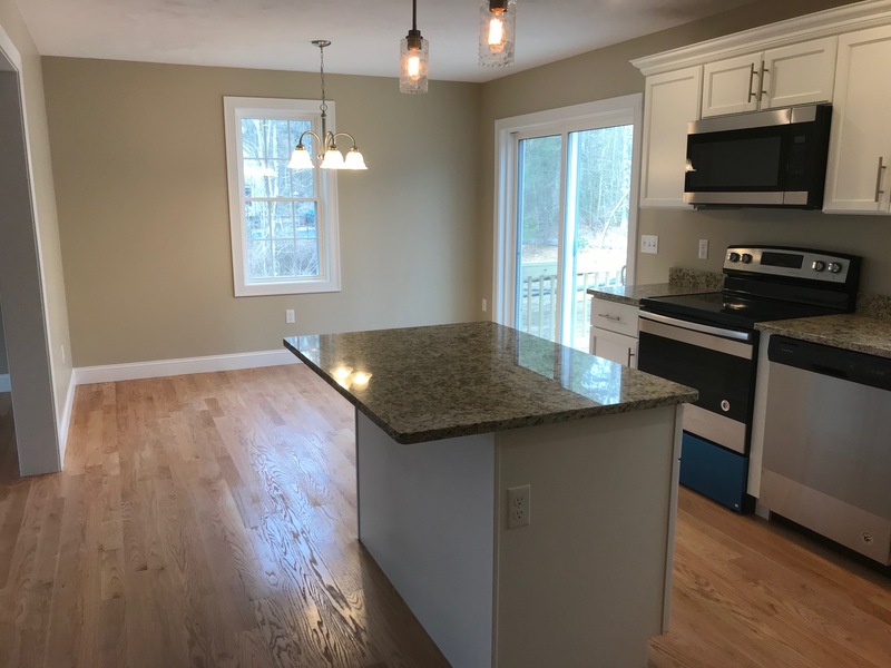 Modern kitchen with granite island, stainless steel appliances, and wooden floors.