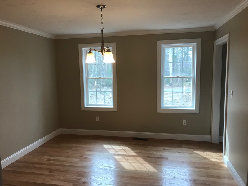 Empty room with hardwood floor, beige walls, two windows, and a ceiling light fixture.