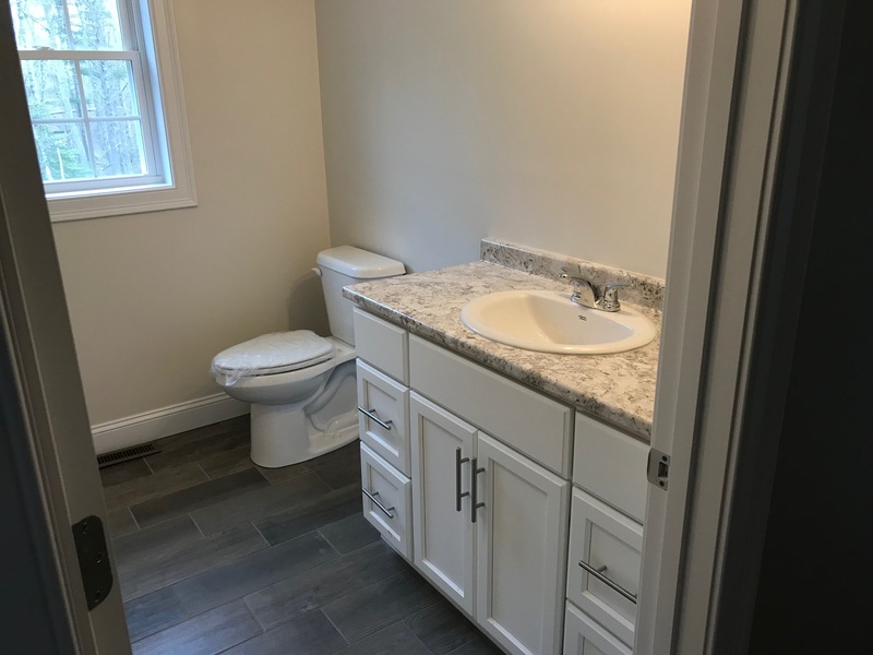 Small bathroom with white vanity, marble countertop, toilet, and window with natural light.