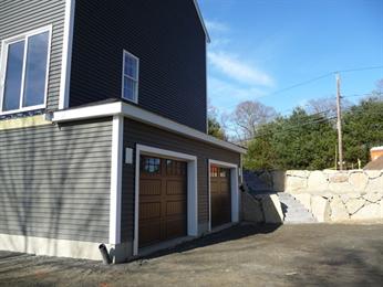 Modern house with two brown garage doors, gray siding, and stone retaining wall outside.