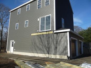 Gray three-story house with a large unfinished opening and lumber stacked in the foreground.