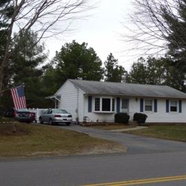 Single-story white house with an American flag and two cars parked in the driveway.