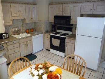 A cozy kitchen with light cabinets, white appliances, and flowers on the table.