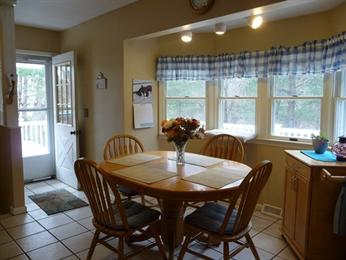 Wooden dining table with four chairs in a kitchen by windows with blue plaid curtains.