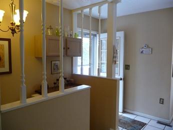 Small entryway with beige walls, white trim, open door, and vertical white spindles.