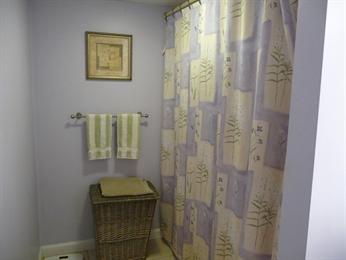 Bathroom with a wicker hamper, striped towels, and a patterned shower curtain.