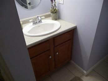 Small bathroom sink with wooden cabinet, faucet, and a potted plant on the countertop.
