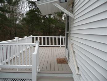 White-railed deck attached to a house, overlooking trees with gray flooring and steps.