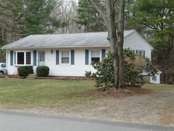 Single-story white house with blue shutters, trees, and a grassy front yard.