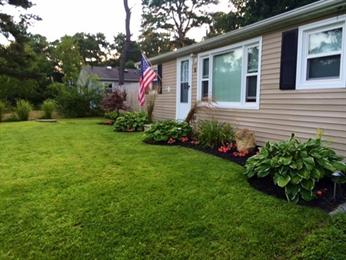 Single-story house with an American flag, tidy lawn, and flower beds in front yard.