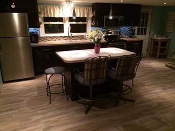 Modern kitchen with island, two chairs, stainless steel appliances, and flower centerpiece.