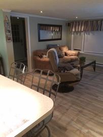 Beige living room with sofa, recliner, glass coffee table, and kitchen counter chairs.