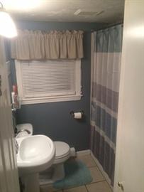 Small bathroom with a white sink, toilet, blue walls, and a shower with a striped curtain.
