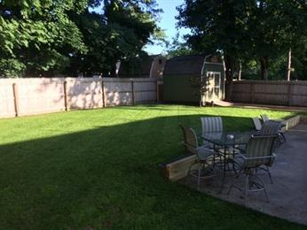 Backyard with green grass, a shed, and patio furniture on a concrete area.