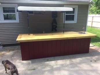 Outdoor bar with a wooden countertop, sink, overhead canopy, and a dog nearby.