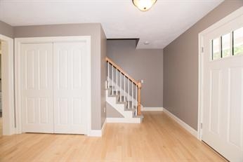 Bright entryway with light wood floors, staircase, closet, and white front door.