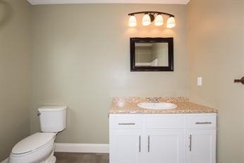 Simple bathroom with a toilet, white vanity, mirror, and overhead light fixture.