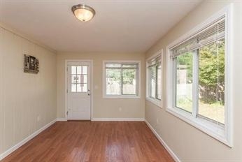 Bright room with wood floors, cream walls, multiple windows, and a white door.