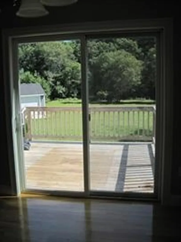 Sliding glass door opens to a wooden deck with a railing and a grassy yard beyond.