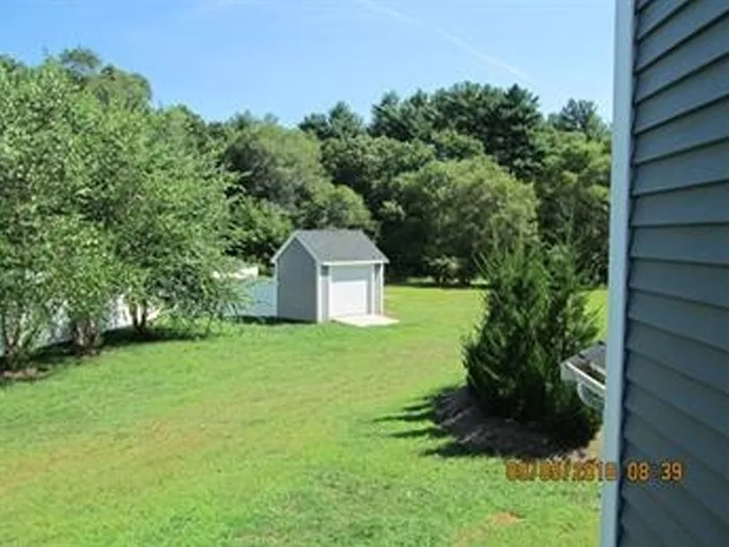 Small gray shed on a grassy lawn with trees and part of a house visible on the right.