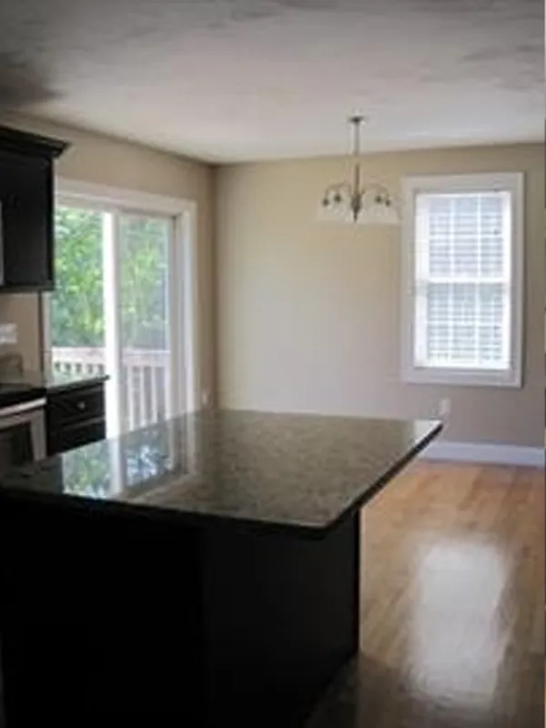 Bright kitchen with a dark granite island, wood floor, window, and sliding glass door.