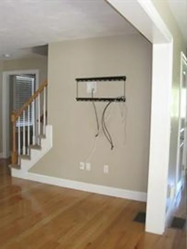 Empty living room with wall-mounted TV bracket, exposed cables, and wooden staircase nearby.