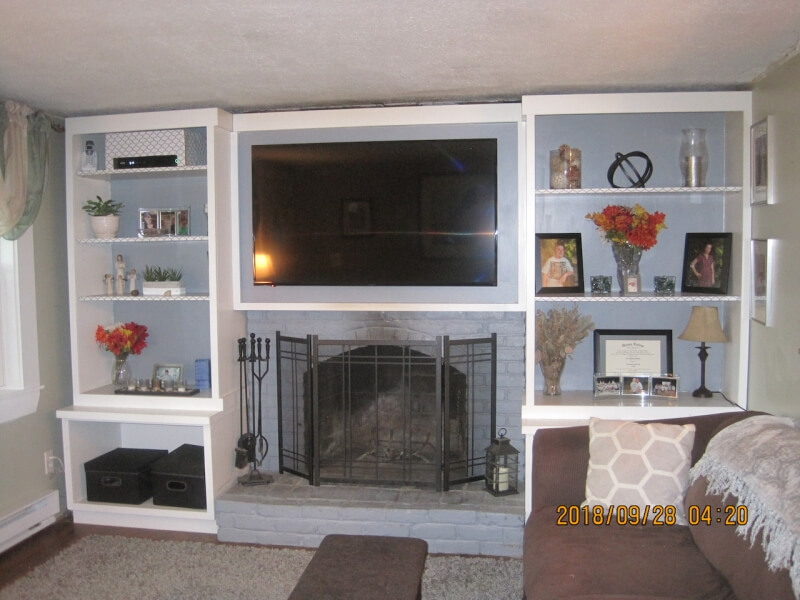 Built-in shelves and a TV surround a fireplace, decorated with flowers and framed photos.