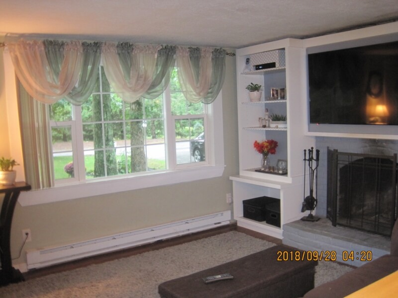 Living room with large window, draped curtains, built-in shelves, and a fireplace.