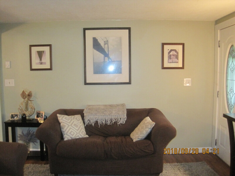 A brown sofa with pillows and a throw, under three framed pictures on a light wall.