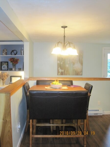 Dining table with four chairs under a hanging light in a cozy, softly lit room.