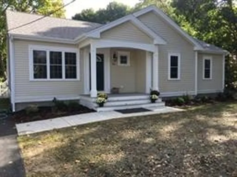Single-story beige house with white trim, front porch, and small garden beds.