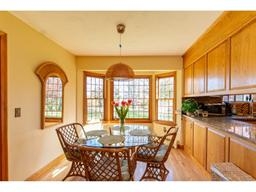 Breakfast nook with glass table, wicker chairs, and bay windows letting in sunlight.