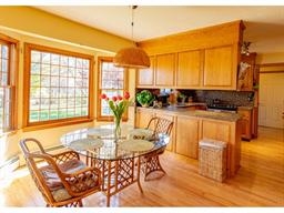 Sunny kitchen with wood cabinets, glass table, and wicker chairs by large windows.