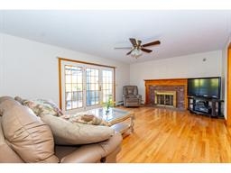 Bright living room with wood floors, fireplace, TV, couch, recliner, and ceiling fan.
