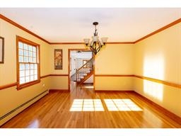 Bright dining room with wood floors, yellow walls, and a chandelier, near a staircase.