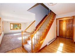 Sunlit entryway with wooden stairs, carpeted living room, and double wooden doors.