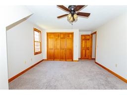 Bright empty room with carpet, wood trim, double closet, window, and ceiling fan.