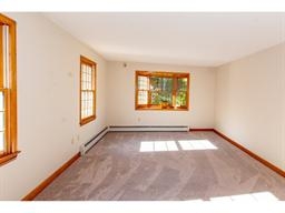 Bright, empty room with beige walls, large windows, and light gray carpet flooring.